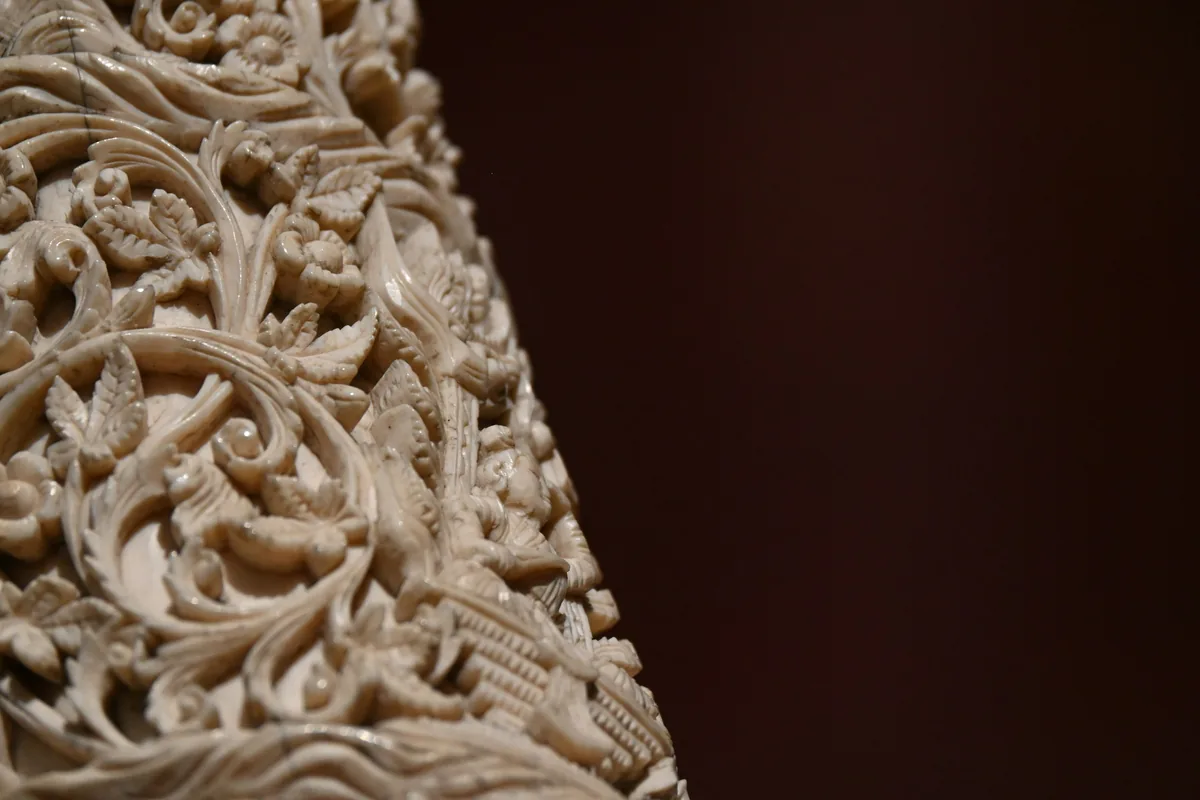 Detalle de una pieza de hueso tallada con motivos vegetales calados y en relieve sobre fondo oscuro